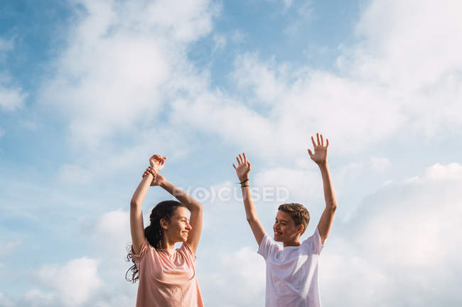 Смеющийся мальчик и девочка стоят с поднятыми вверх руками перед небом — стоковое фото