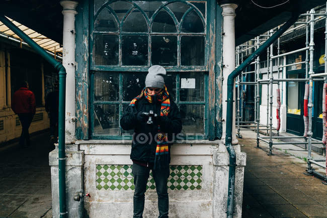 Uomo appoggiato alla finestra grungy di legno mentre si utilizza la fotocamera sulla strada della città vecchia, Oporto, Portogallo — Foto stock