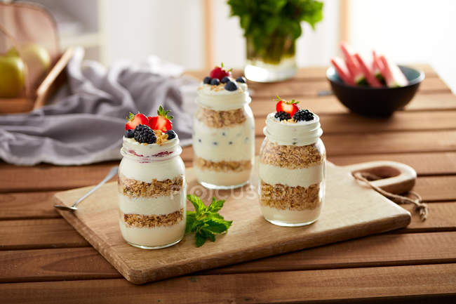 Glass jars with granola and yogurt on wooden board — Stock Photo