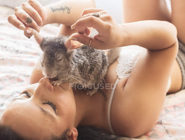 Young woman lying in bed with chinchilla — Stock Photo