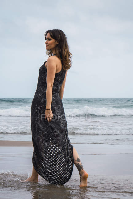 Элегантная женщина в черном платье прогулка по пляжу — стоковое фото