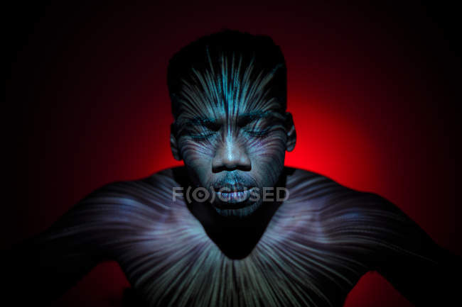 Uomo etnico senza emozioni in piedi con linee di luce sul corpo — Foto stock