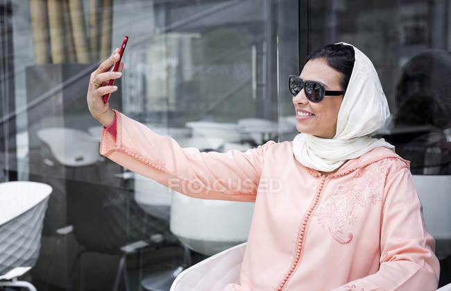 Марокканская женщина с хиджабом и типичным арабским платьем делает селфи в кафе — стоковое фото