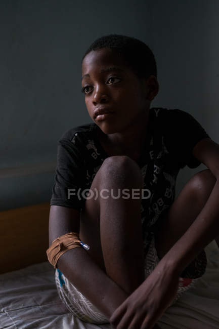 ANGOLA - ÁFRICA - 5 DE ABRIL DE 2018 - Menino negro pensativo sentado na cama em casa e olhando para longe — Fotografia de Stock