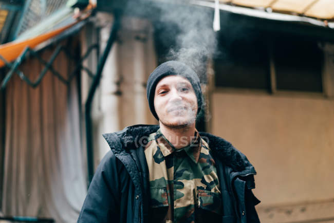 Porträt eines gutaussehenden jungen Mannes, der auf der Straße steht und raucht — Stockfoto