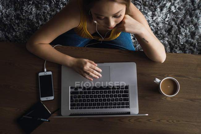 Mujer usando el ordenador portátil en la mesa con taza y teléfono inteligente - foto de stock