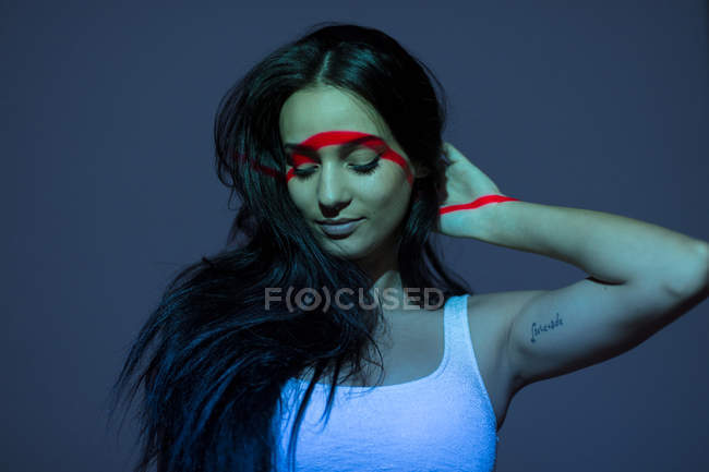 Jeune femme séduisante avec ligne rouge sur le visage et le corps debout sur fond gris — Photo de stock