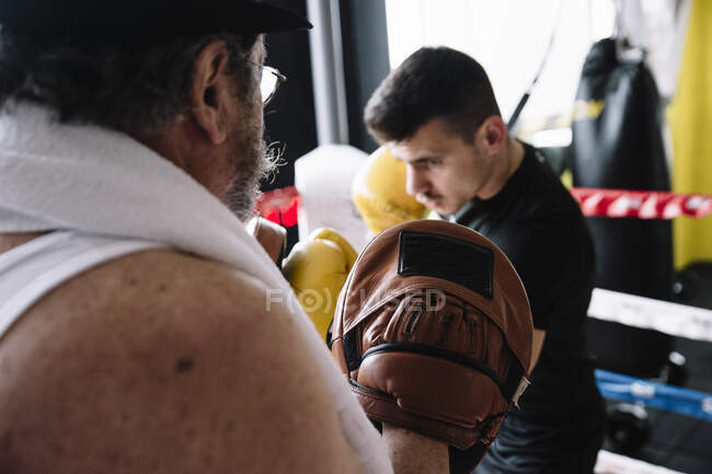 Вид збоку боксерський чоловік ударяє рукавички тренера в спортзалі . — стокове фото