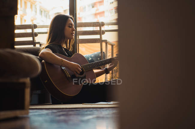 Жінка, сидячи на підлозі будинку грати на гітарі — стокове фото