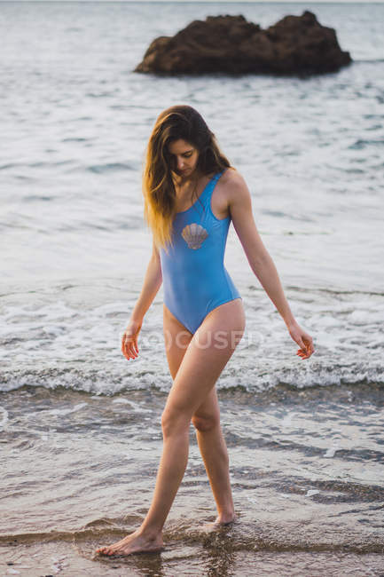 Mujer bonita en traje de baño azul caminando en la playa - foto de stock