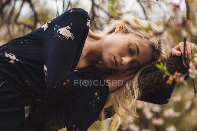 Young blonde woman leaning on blooming tree and relaxing with eyes closed in nature — Stock Photo