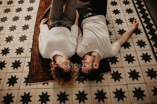 Joven pareja acostada en la alfombra y mirándose - foto de stock