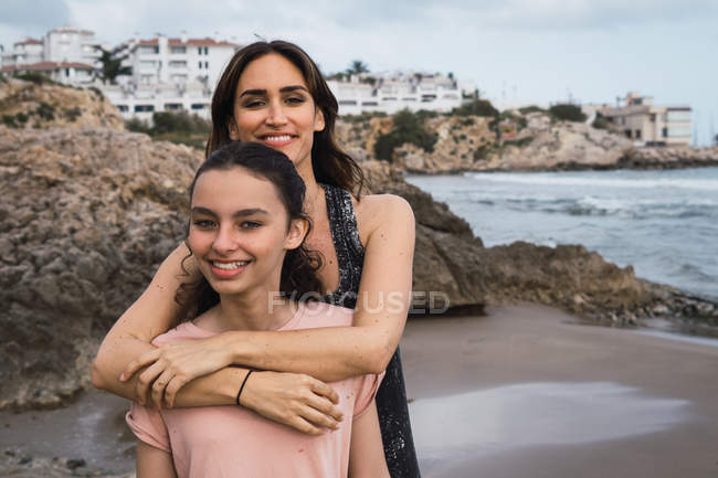 Женщина обнимает улыбающуюся дочь на берегу моря летом — стоковое фото