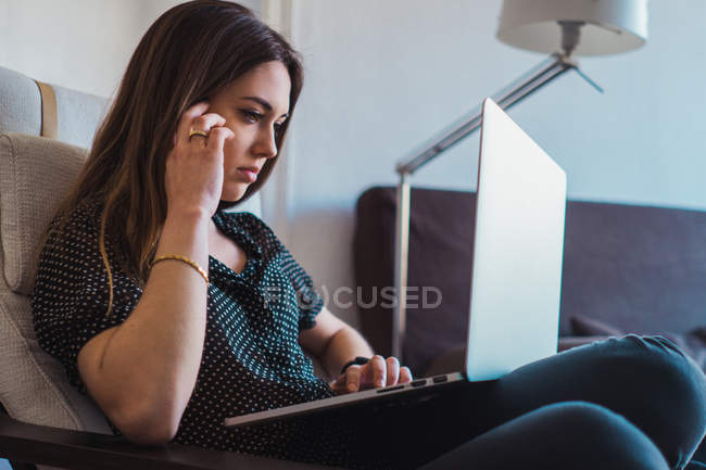 Mulher pensativa usando laptop em poltrona em casa — Fotografia de Stock