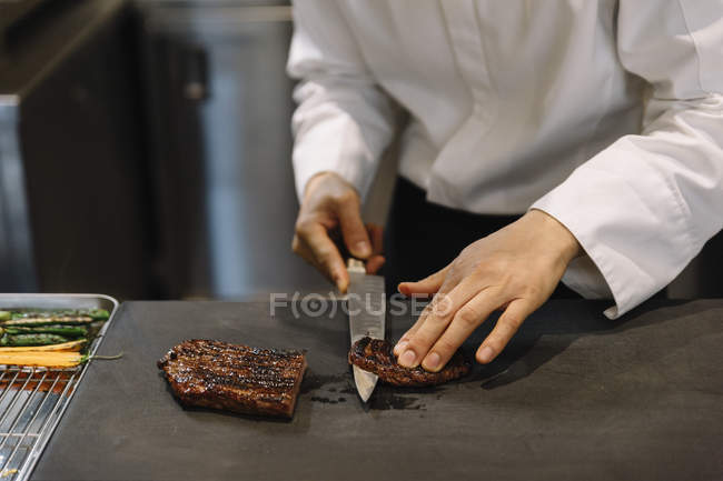 Шеф-повар нарезает мясо на гриле в ресторане — стоковое фото
