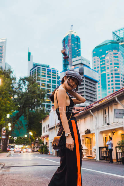 Азиатка в стильной одежде идет по освещенной улице в сумерках — стоковое фото