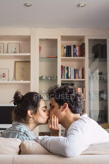 Joven hombre y mujer sentado en el sofá en la sala de estar y besar - foto de stock