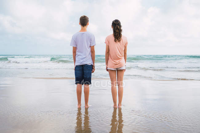 Вид сзади на мальчика и девочку, стоящих на пляже — стоковое фото