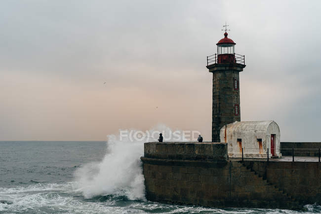 Torre beacon no cais no oceano ondulado, Porto, Portugal — Fotografia de Stock