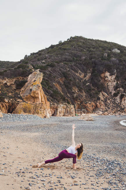 Femme en forme faisant de l'exercice sur la plage rocheuse — Photo de stock