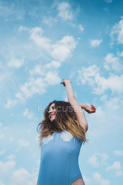 Cheerful young woman in blue swimsuit standing against blue sky — Stock Photo