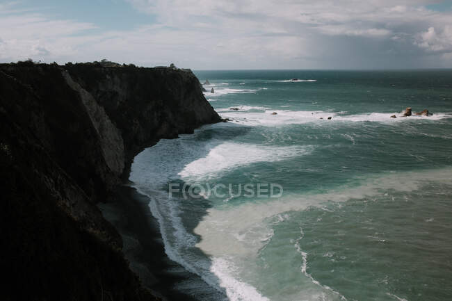 Vista para a rocha costeira e oceano azul ondulado em dia nublado. — Fotografia de Stock