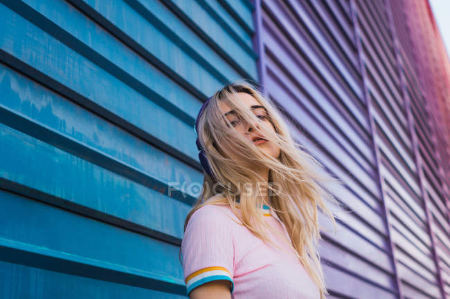 Молода блондинка слухає музику на барвистій стіні — стокове фото