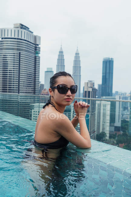 Азіатський жінка розслаблюючим у басейні з ультрасучасні хмарочоси на фоні — стокове фото