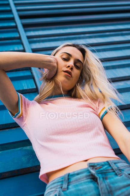 Portrait of young blonde woman leaning on blue wall on street — Stock Photo