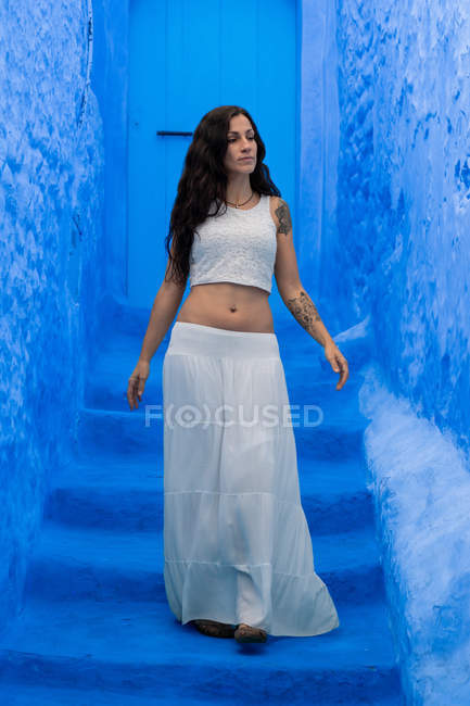 Donna vestita con top bianco e gonna lunga in piedi su strada blu tinta, Marocco — Foto stock