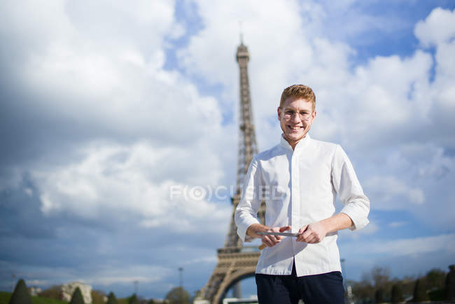 Улыбающийся рыжеволосый повар с ножами, стоящий перед Эйфелевой башней в Париже — стоковое фото