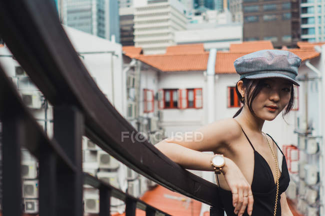 Jeune femme asiatique dans des vêtements élégants penché sur la clôture en ville — Photo de stock