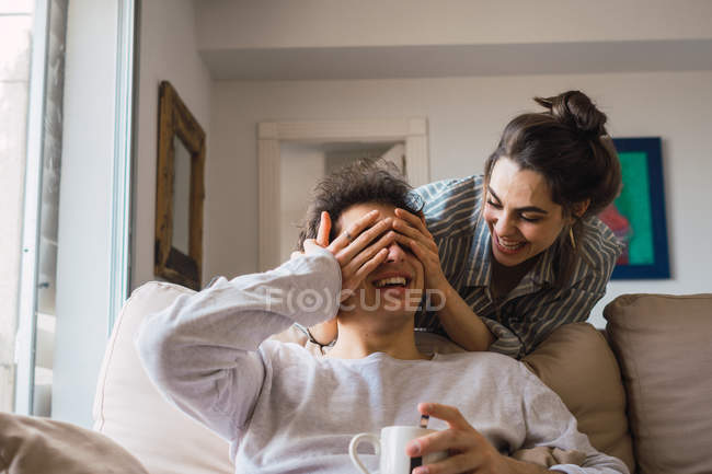 Mujer alegre en pijama cerrando los ojos al novio con las manos - foto de stock