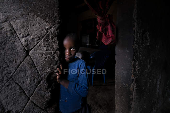 ANGOLA - ÁFRICA - 5 de abril de 2018 - Niño africano de pie a la entrada de la casa gruñona y mirando a la cámara - foto de stock