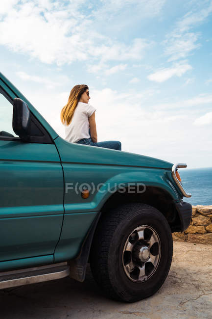 Женщина, сидящая на багажнике машины у моря — стоковое фото