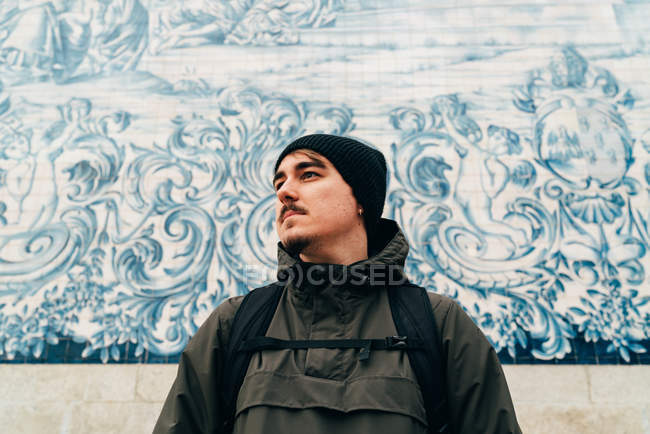 Mann in warmer Kleidung steht an weißer Wand mit blauem Ornament — Stockfoto