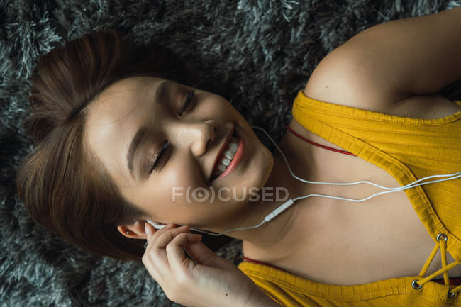 Femme souriante avec écouteurs couchés sur le sol — Photo de stock