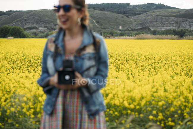 Frau mit Sonnenbrille lacht in der Natur und hält Retro-Kamera in der Hand — Stockfoto