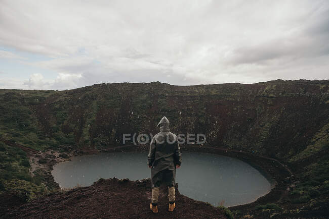 Visão traseira do turista em pé no lago com as mãos nos bolsos e olhando para o lago. — Fotografia de Stock