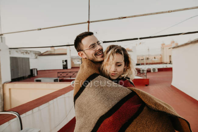 Pareja abrazando con manta en terraza - foto de stock