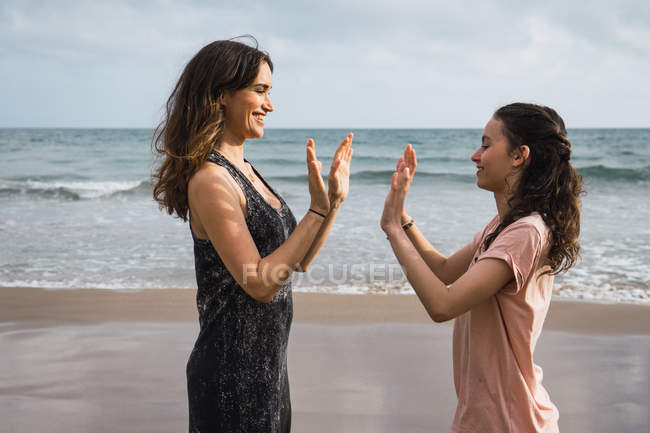 Sonriente madre con hija jugando pat-a-cake en la orilla del mar de verano - foto de stock