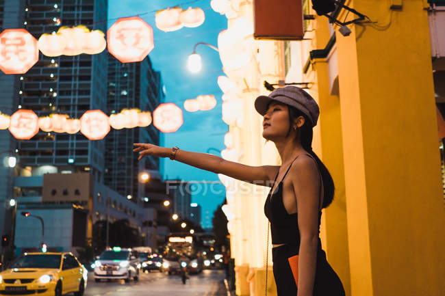 Stylische junge asiatische Frau steht auf der Straße und fängt Taxi am Abend — Stockfoto
