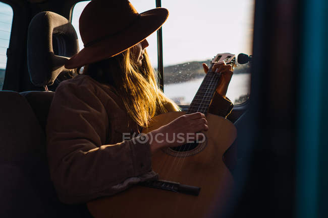 Atractiva joven tocando la guitarra y sentada en coche en la naturaleza - foto de stock