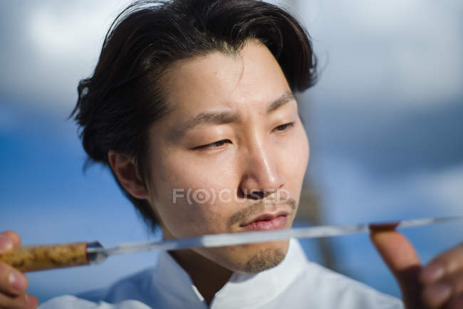 Chef japonés comprobando cuchillo delante del cielo azul - foto de stock