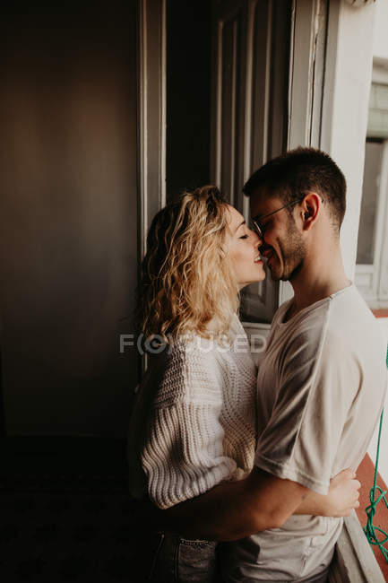 Couple affectueux embrassant à la fenêtre à la maison — Photo de stock