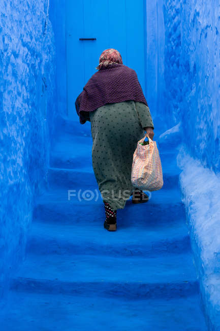 Old woman climbing the blue stairs in Morocco — Stock Photo
