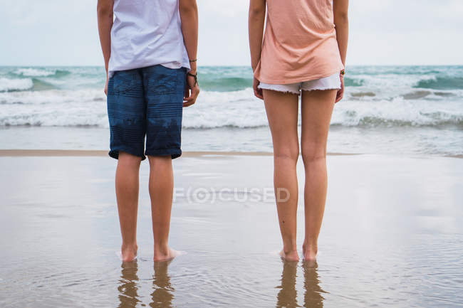 Piernas de amigos adolescentes de pie en la playa - foto de stock