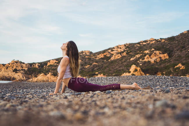 Fit woman exercising on rocky beach — Stock Photo