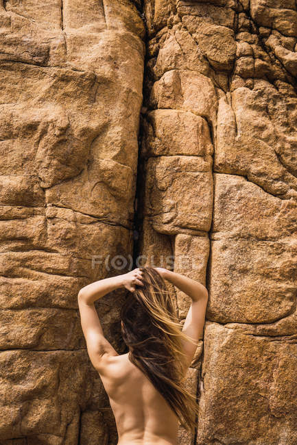 Visão traseira da mulher nua em pé na frente da parede da montanha áspera — Fotografia de Stock