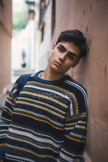Молодой уверенный в себе подросток в свитере стоит на городской улице и смотрит в камеру . — стоковое фото